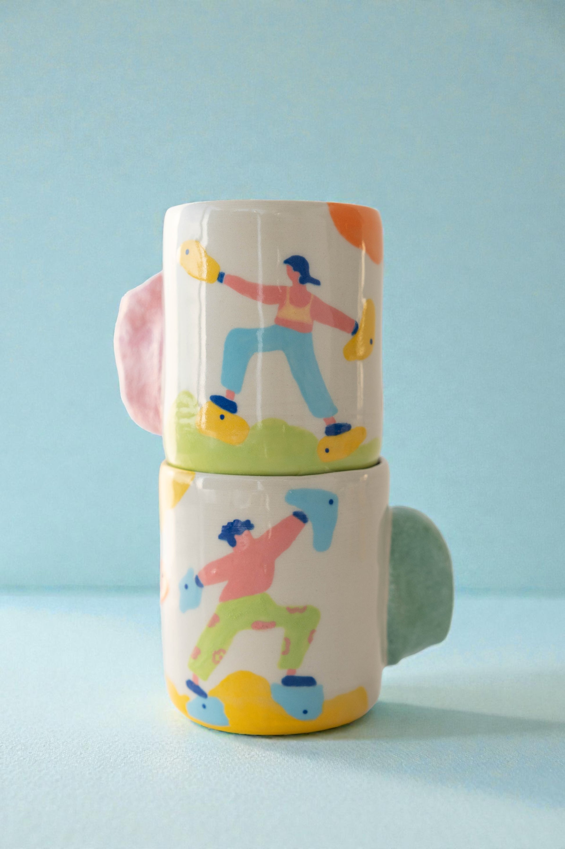 Two stacked ceramic cups with colorful illustrations of people rock clibming on a light blue background.