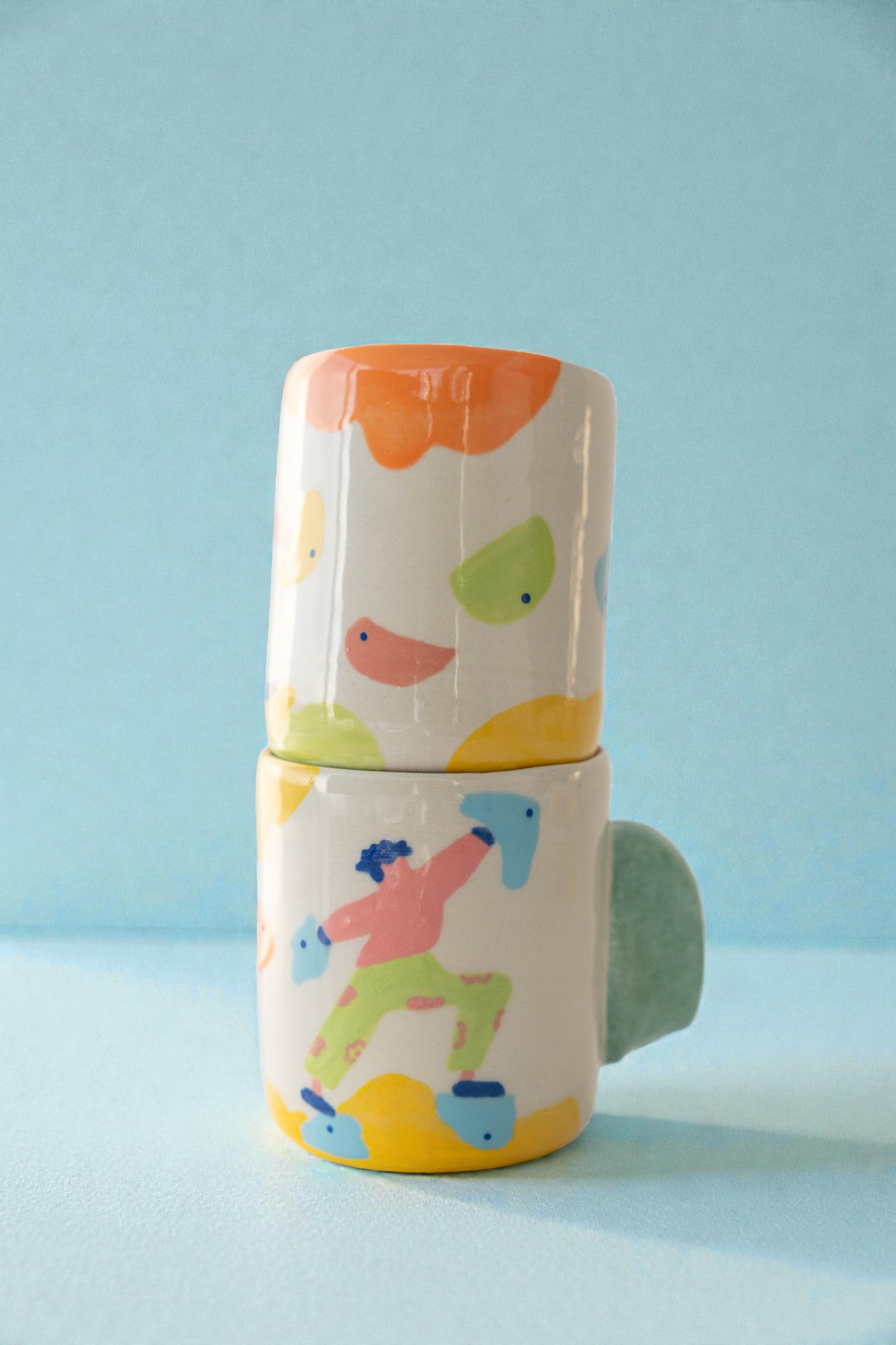 Stack of colorful ceramic cups with simple illustrations on a light blue background