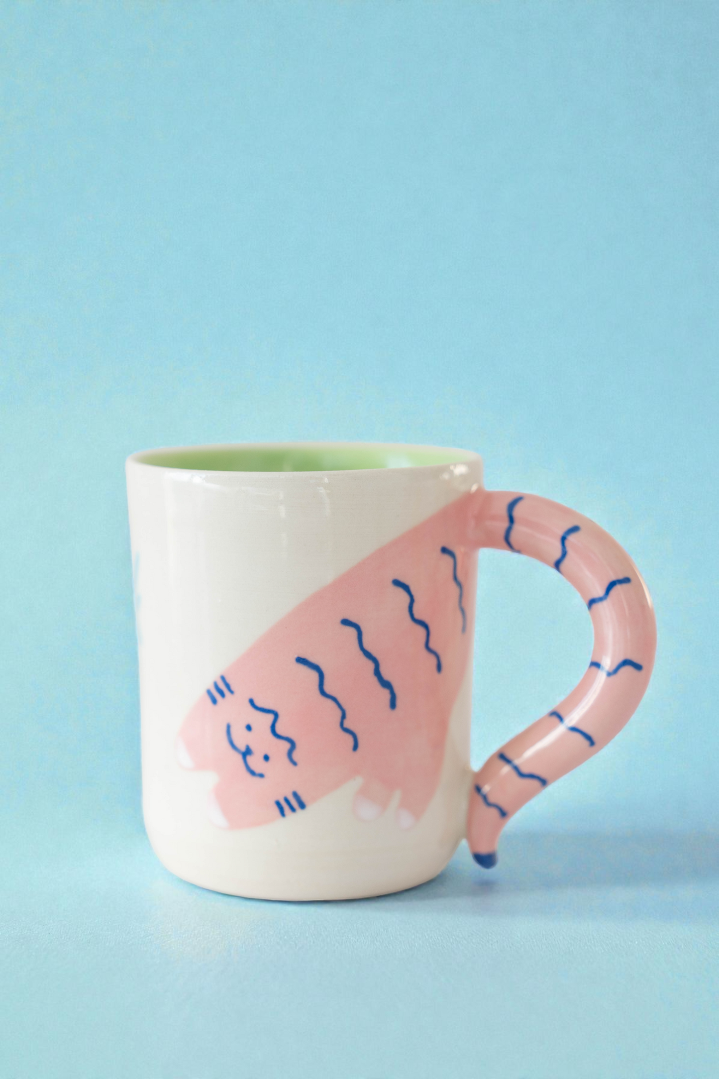Ceramic mug with pink handle and cat design on a light blue background