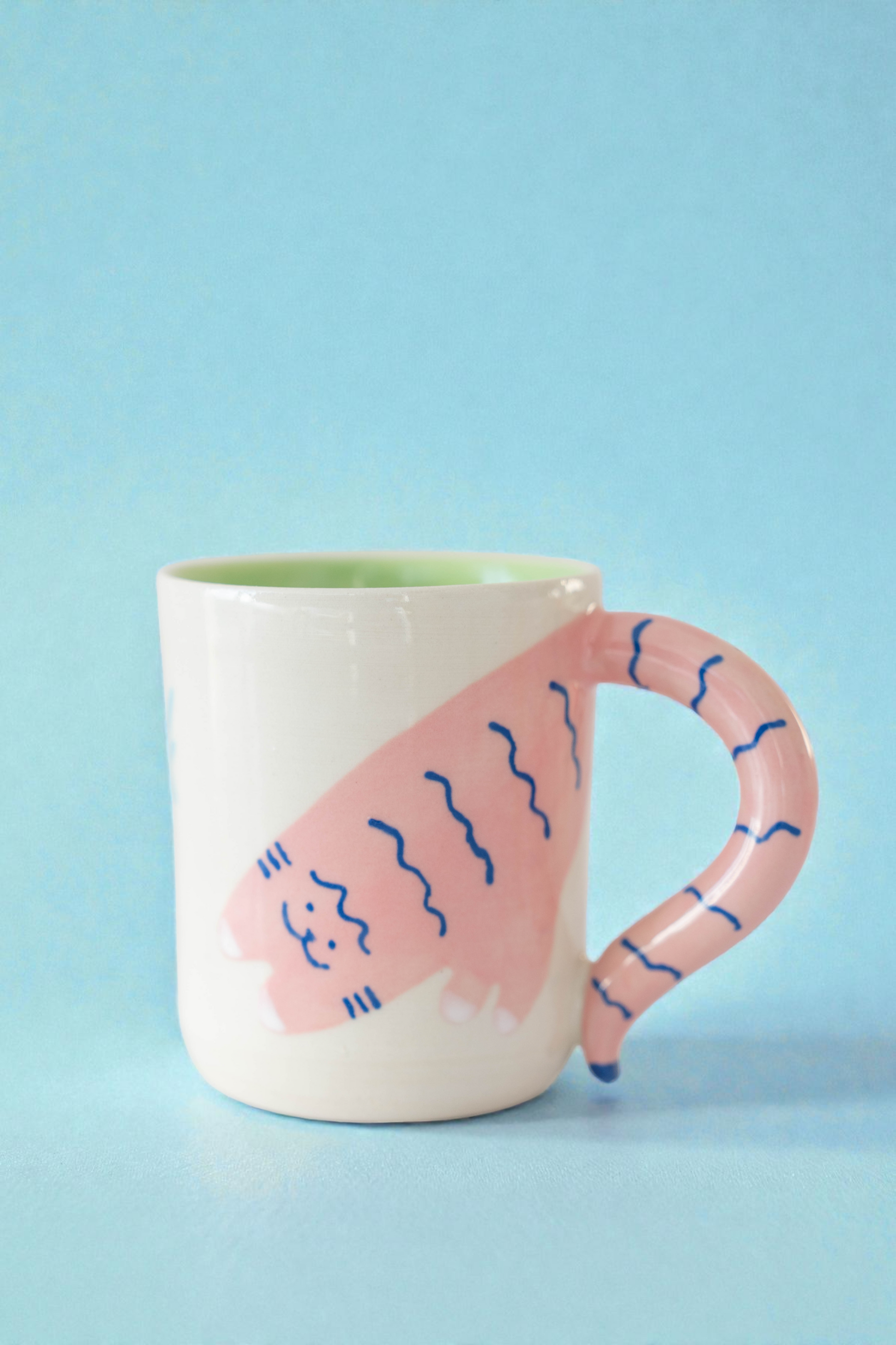 Ceramic mug with pink handle and cat design on a light blue background