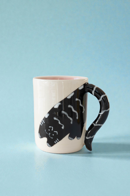 Mug with a black cat design on a white handle against a light blue background
