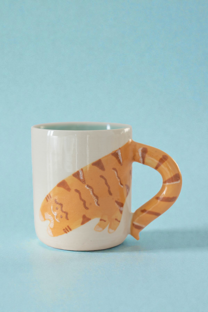 Ceramic mug with a tabby cat-shaped handle on a light blue background